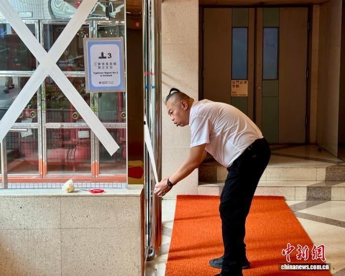 Nhân viên ban quản lý một khu dân cư tại Hồng Kông sử dụng băng dính gia cố cửa ra vào và cửa sổ trước bão Wipha. Ảnh: Chinanews