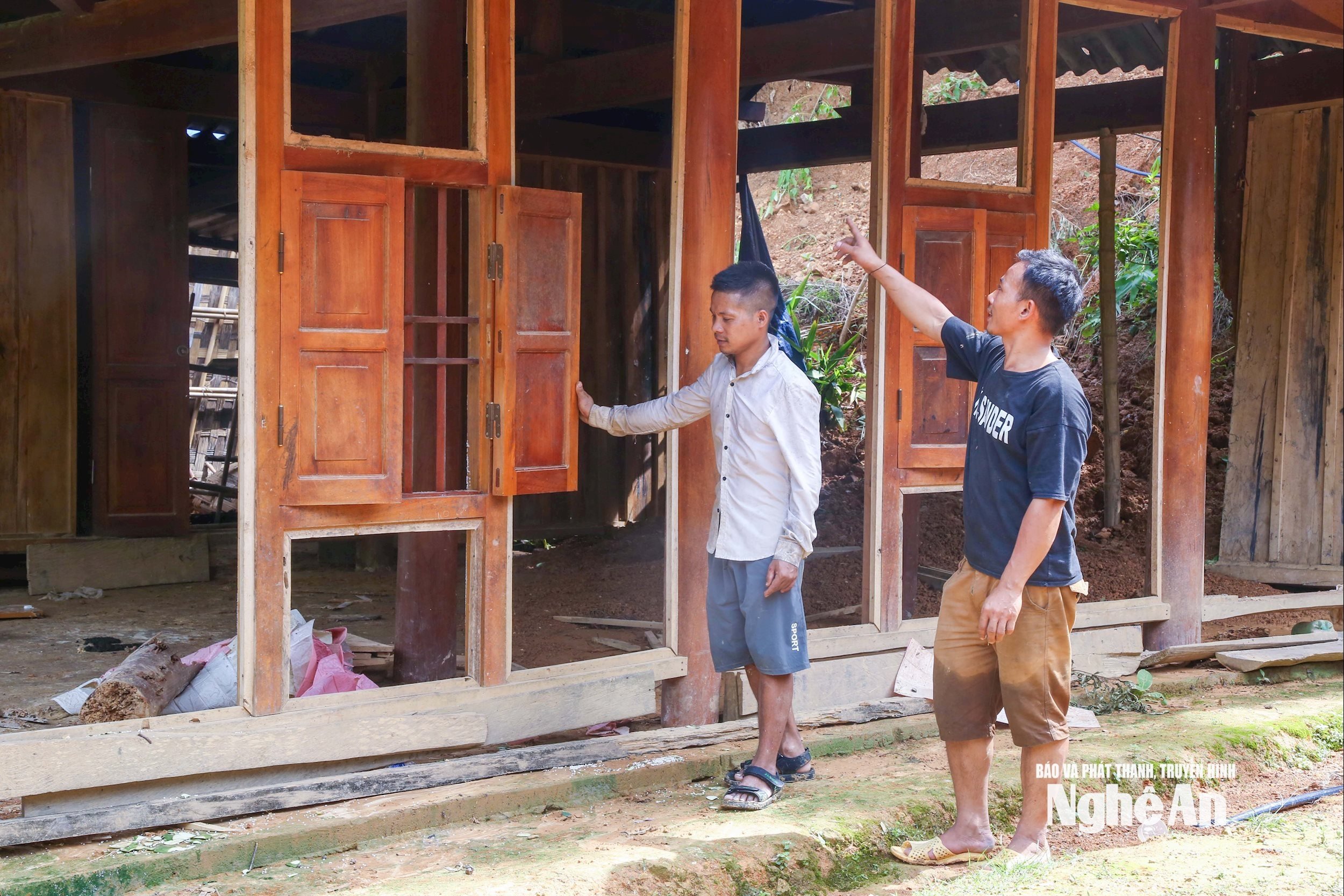 Dẫn phóng viên đến ngôi nhà bị đổ sập hoàn toàn của mình ở cạnh sườn núi, Moong Văn Hải (áo xanh) kể lại trận lũ diễn ra vào đêm 23/7/2025: “Lũ về trong đêm, nên gia đình phải rất vất vả sơ tán đồ đạc. Lúc ấy trong bản ai cũng phải lo cho nhà mình nên rất ít nhân lực hỗ trợ. ”Người đàn ông 32 tuổi cho hay, vợ chồng anh làm ngôi nhà gỗ này từ năm 2024, hiện vẫn nợ 100 triệu đồng. Ảnh: Đình Tuyên