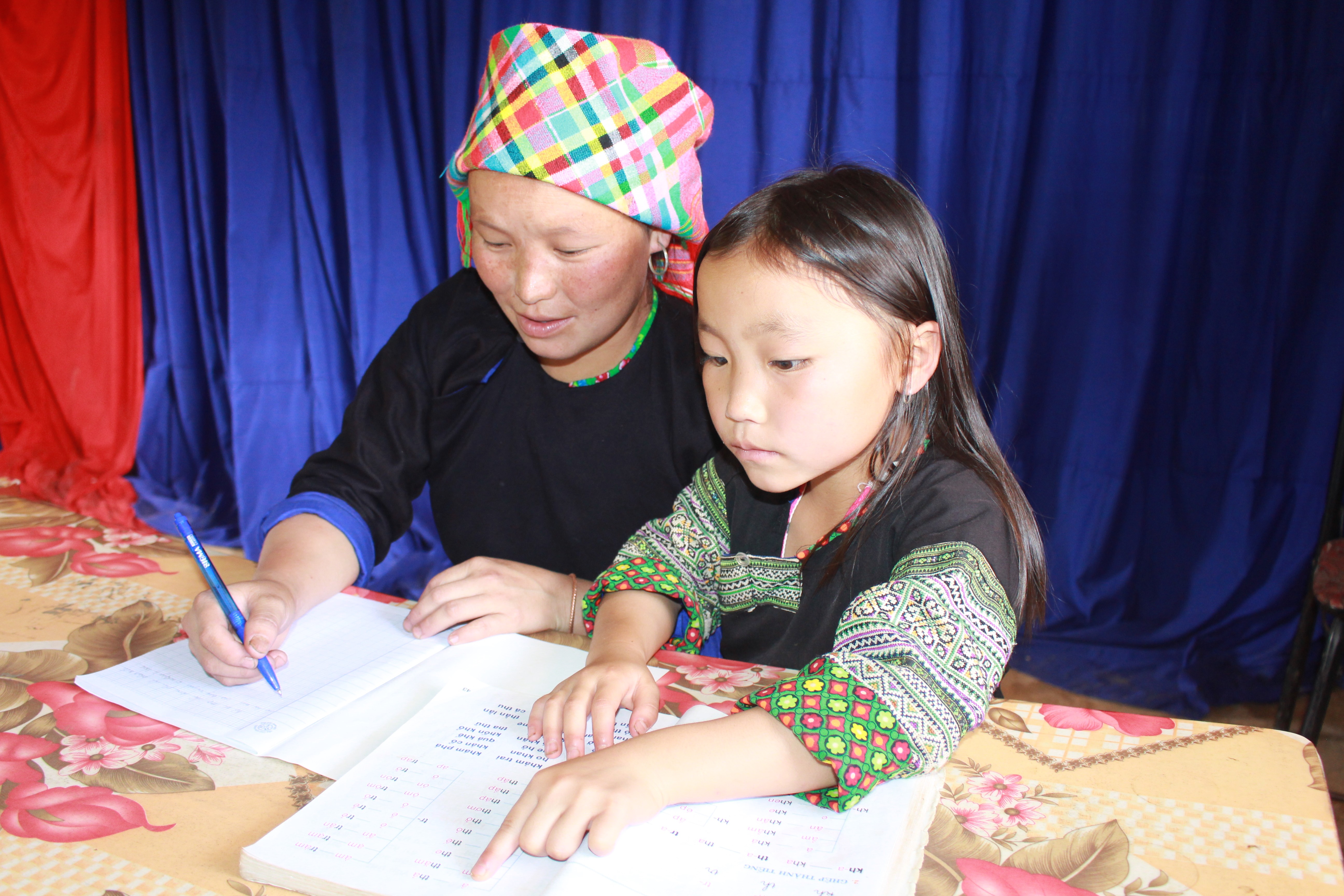 Một em bé Mông dạy mẹ tập viết chữ.