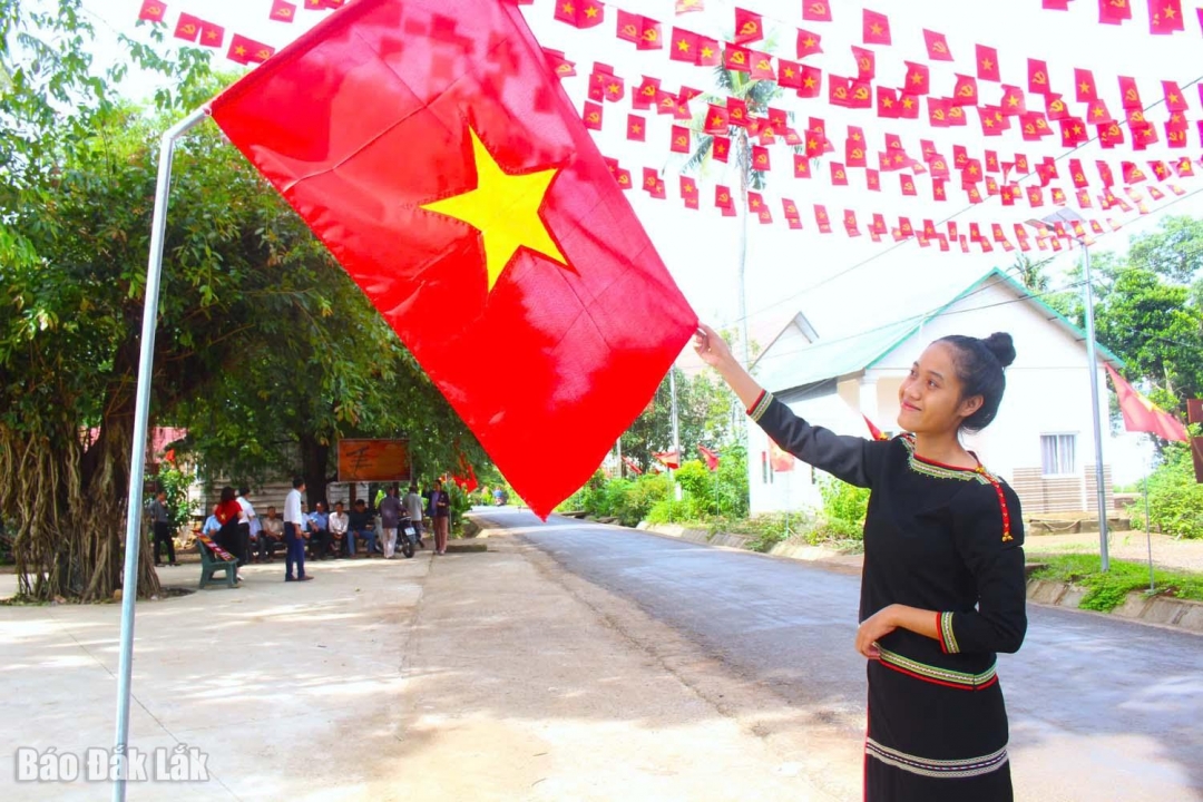 An Ede girl next to the National Flag Pride 2025 project of the People's Committee of Hoa Phu commune.