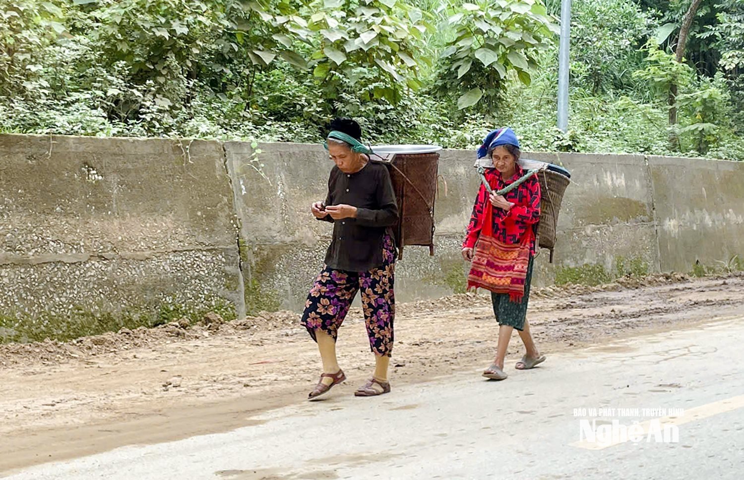 Hai cụ bà người Thái với dáng người lom khom, chiếc gùi tre vẫn còn đeo trên lưng. Trên con đường làng còn loang lổ bùn đất, từng bước chân chậm rãi của các cụ như nhịp sống vùng cao đang dần hồi sinh sau thiên tai. Ảnh: Đình Tuân