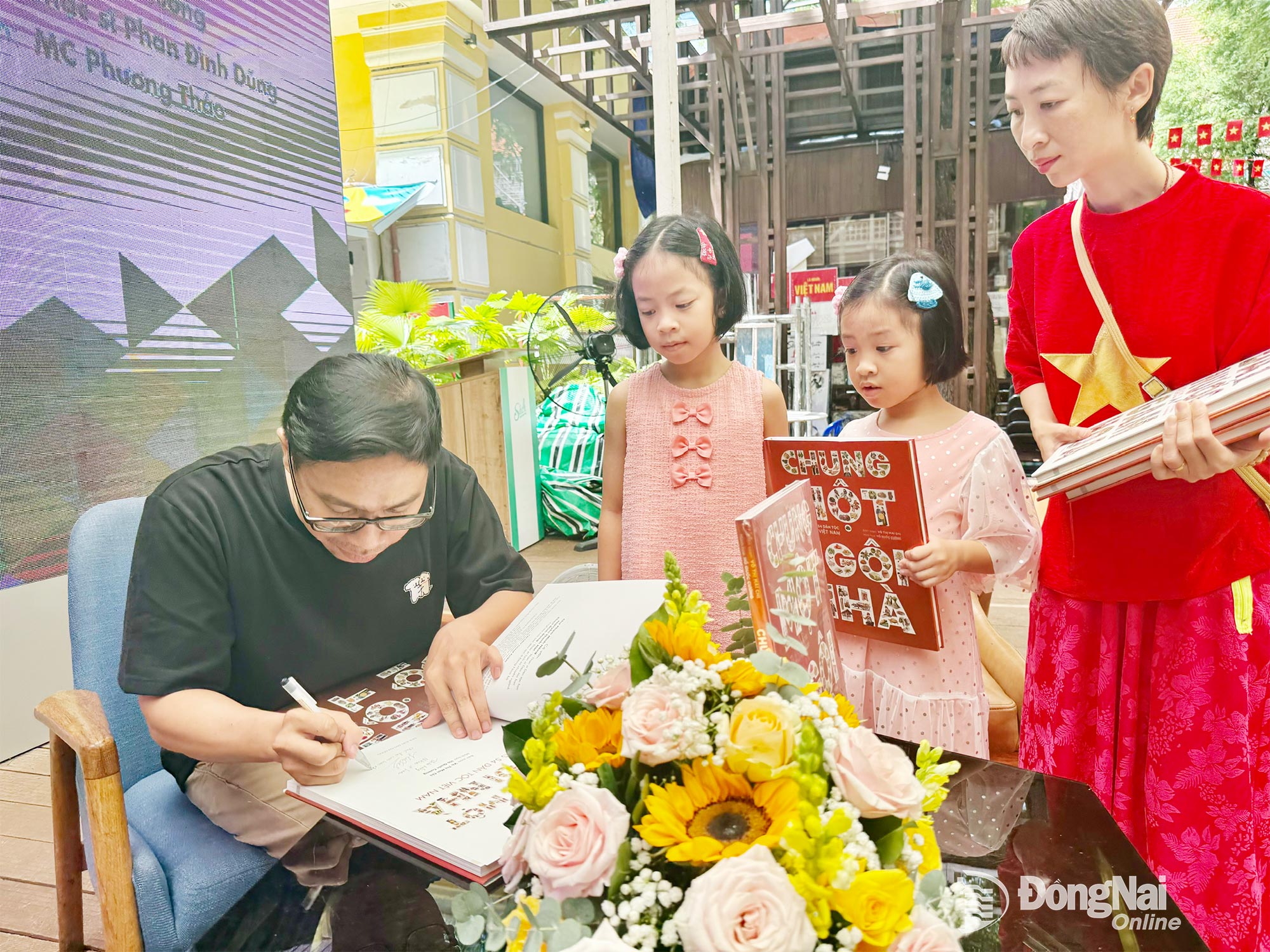 វិចិត្រករ Ho Quoc Cuong ចុះហត្ថលេខាជូនមិត្តអ្នកអានវ័យក្មេងក្នុងពិធីសម្ភោធសៀវភៅ Chung mot ngoi nha នៅវិថីសៀវភៅទីក្រុងហូជីមិញ។