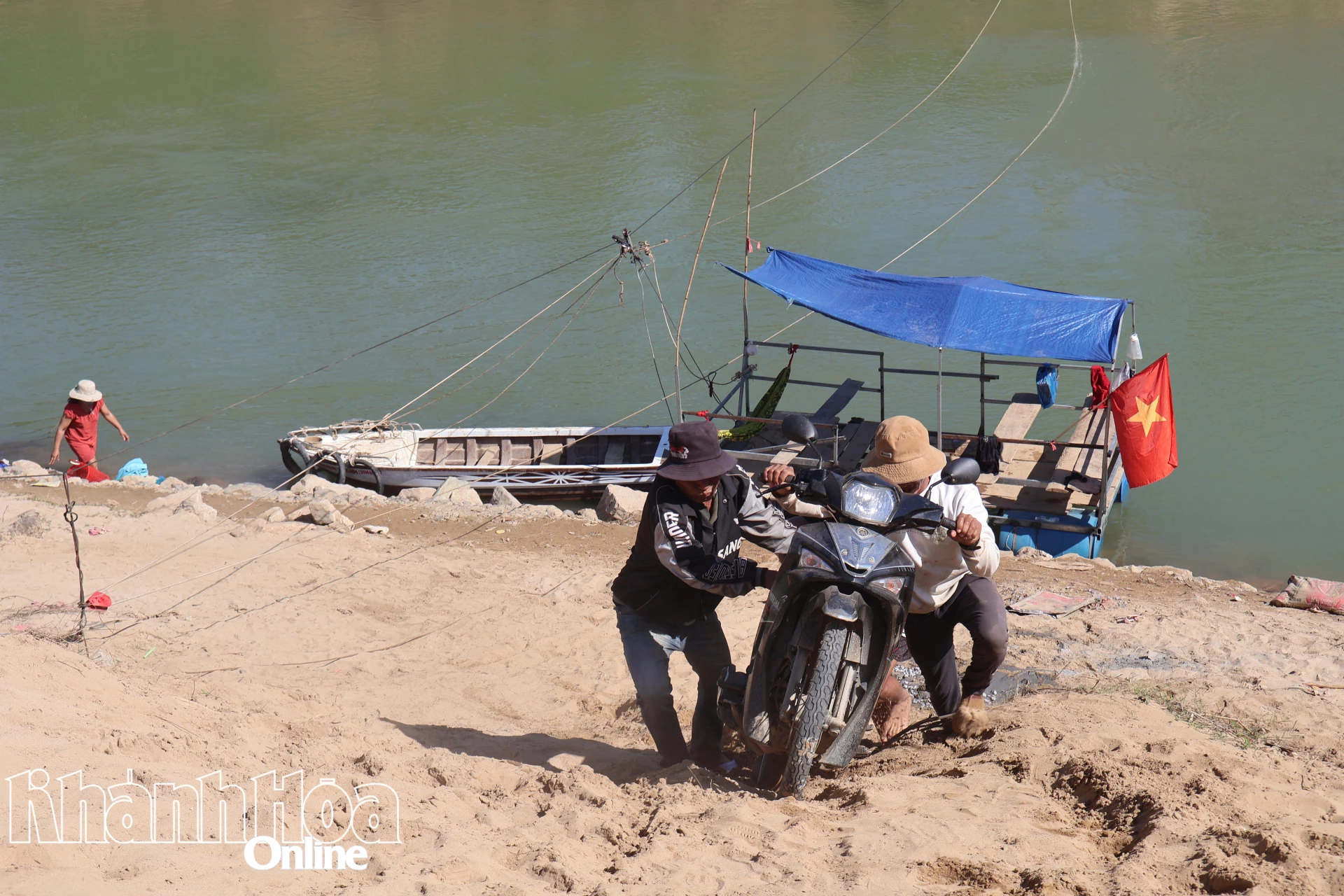 People in Khánh Vĩnh push their motorbikes up after crossing the river.