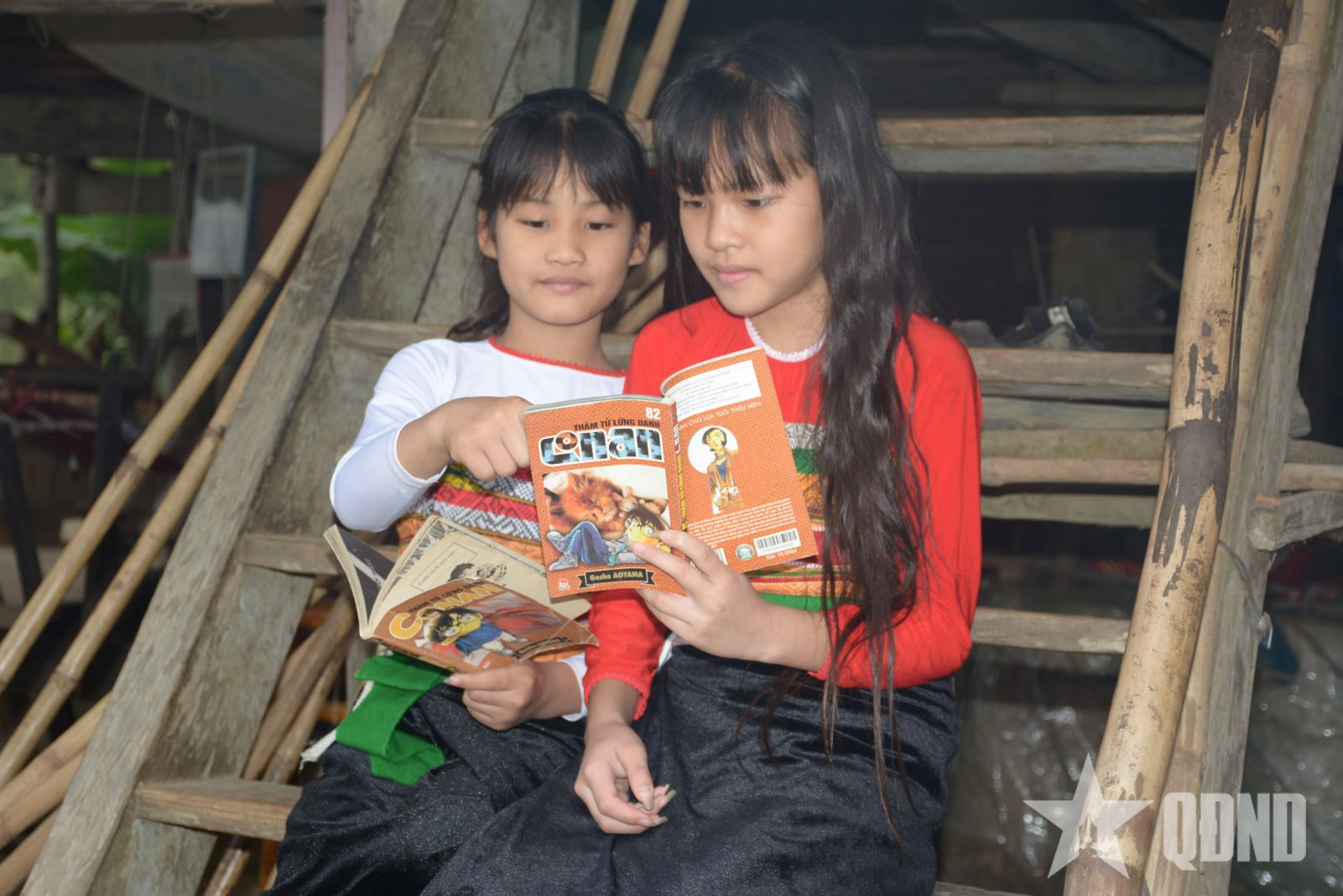 Trong khi bạn bè chơi các trò chơi dân gian thì hai em nhỏ chọn cho mình nơi yên tĩnh, cùng nhau đọc truyện tranh.