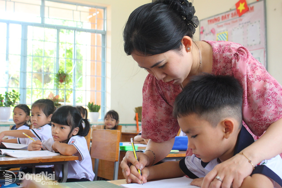 Cô Trương Mỹ Ngọc (giáo viên chủ nhiệm lớp 1/3, Trường Tiểu học Đinh Bộ Lĩnh) giúp học sinh làm quen với nét chữ tại buổi học đầu tiên. Ảnh: Đoàn Phú