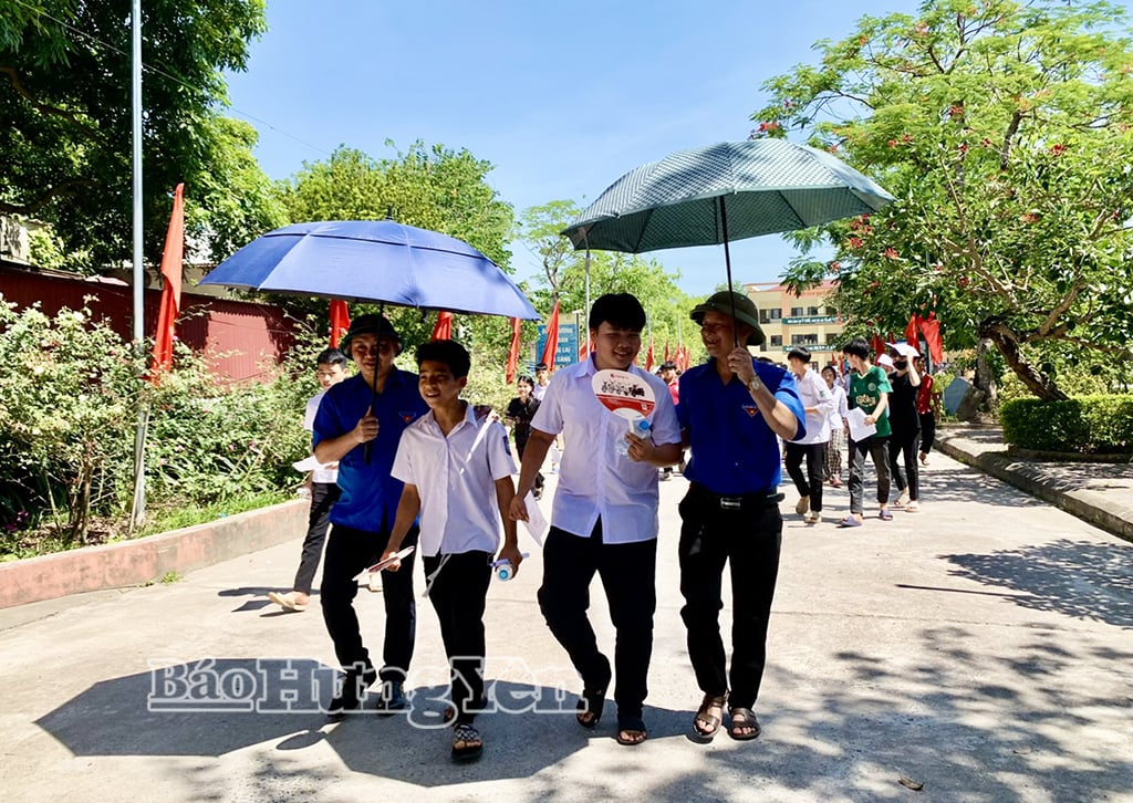Unga volontärer från kommunen Hoang Hoa Tham använde paraplyer för att skydda kandidater från solen vid Tien Lu High Schools examenscenter.