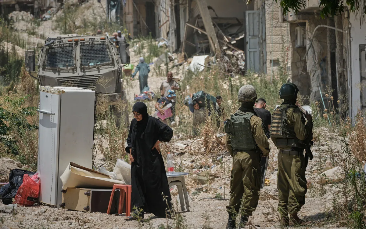 Người dân Palestine thu gom đồ đạc tại trại tị nạn Tulkarem ở Bờ Tây, trong khi binh lính Israel đứng gần đó, ngày 17/6/2026 (Ảnh: AP)